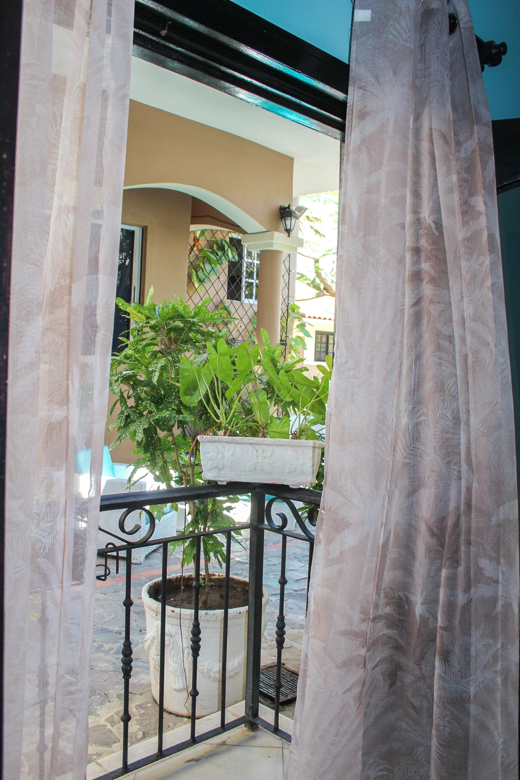 A balcony with a potted plant, a metal railing, and a view of a building with a beige facade.