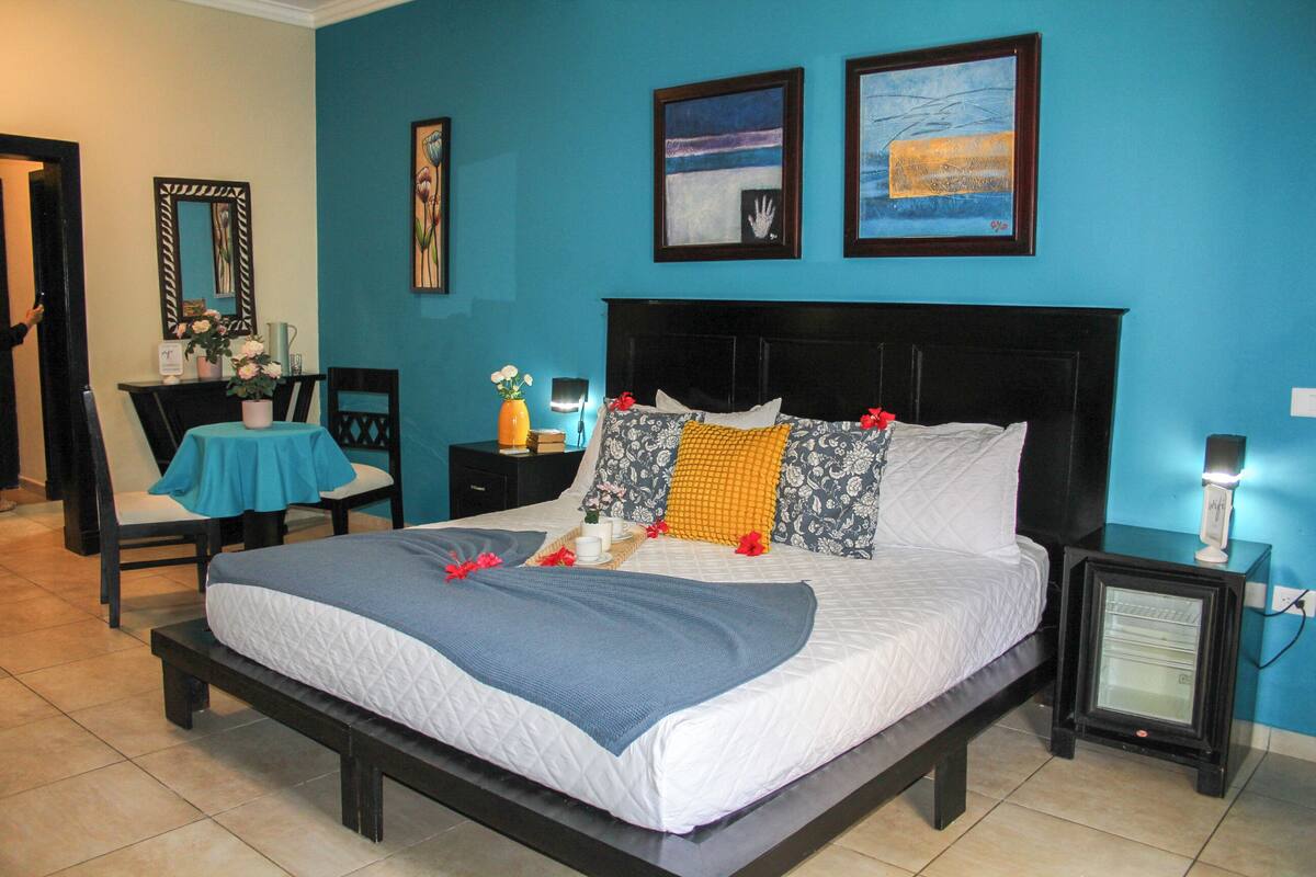 A neatly made bed with a blue blanket, a bedside table with a lamp, and artwork on the walls.