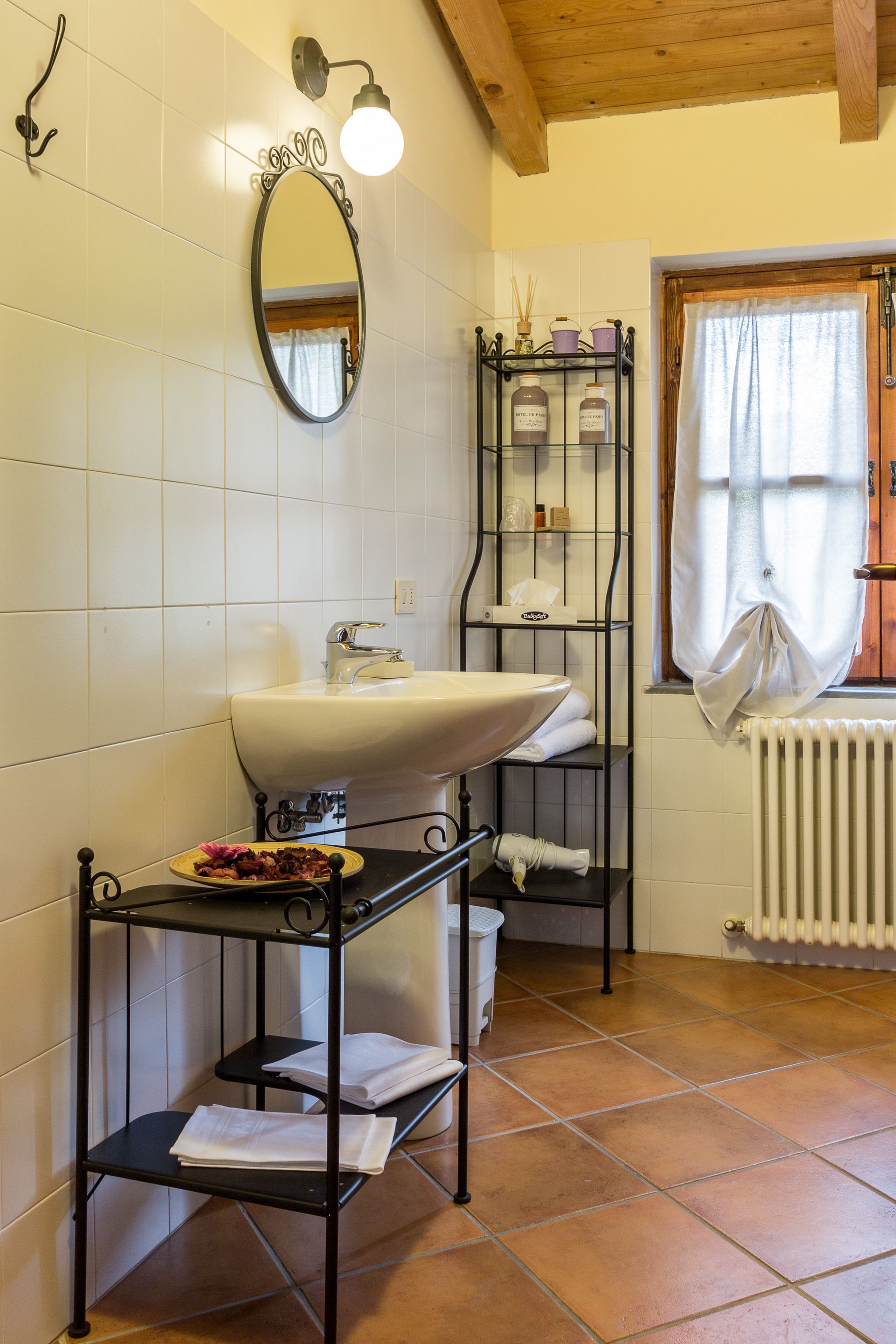 Ein Badezimmer mit einem weißen Waschbecken, einem Spiegel, einer Ablage für Toilettenartikel und einem Fenster mit Vorhängen.