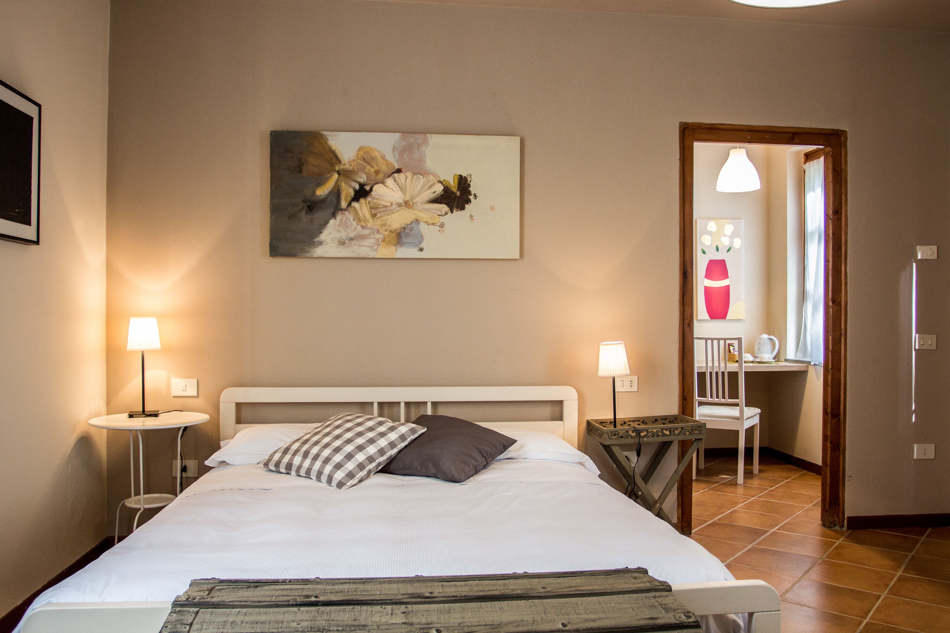 A neatly arranged bedroom with a bed, bedside tables, a chair, and a painting on the wall.