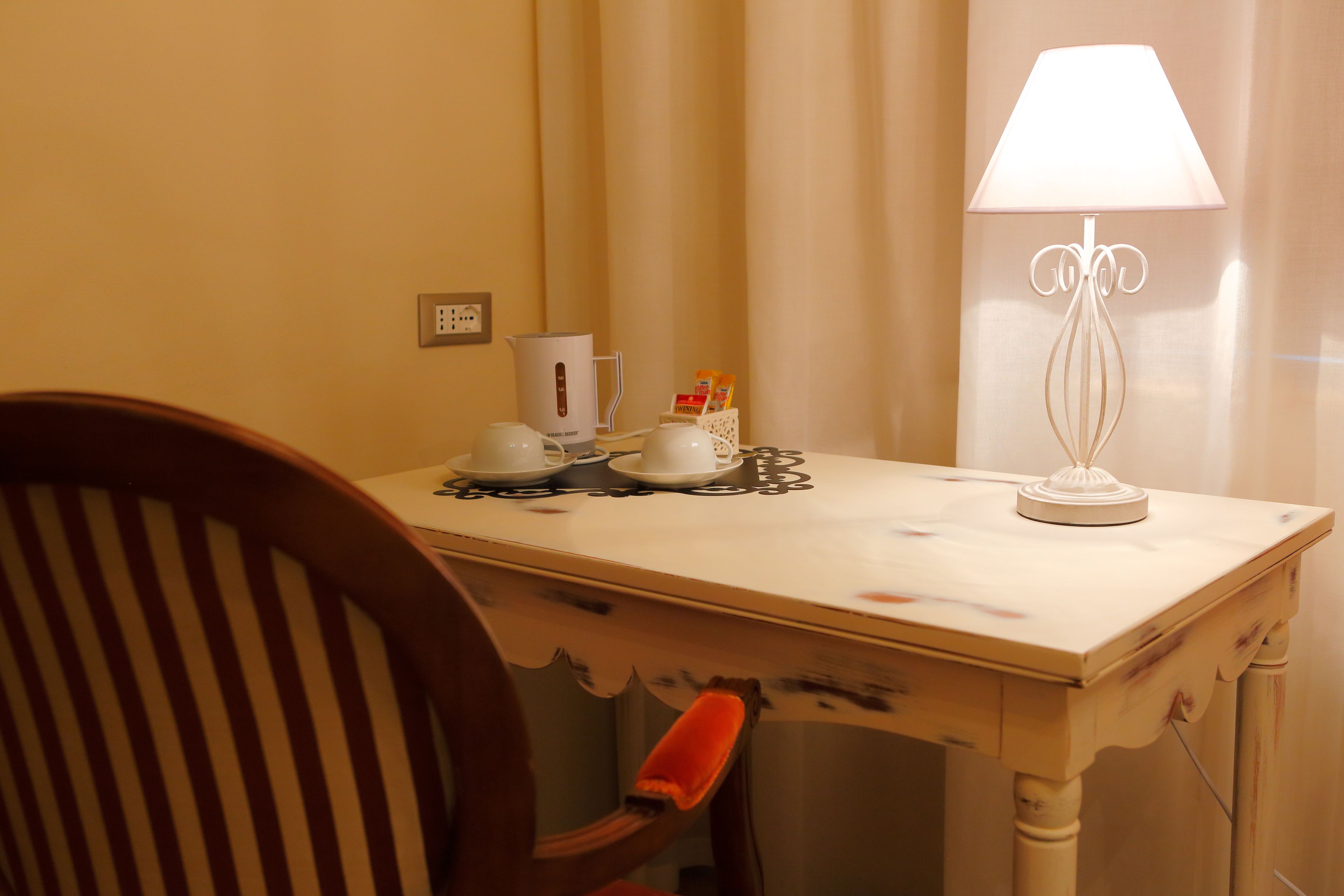 A small table with a white lamp, a coffee maker, and a cup of coffee.