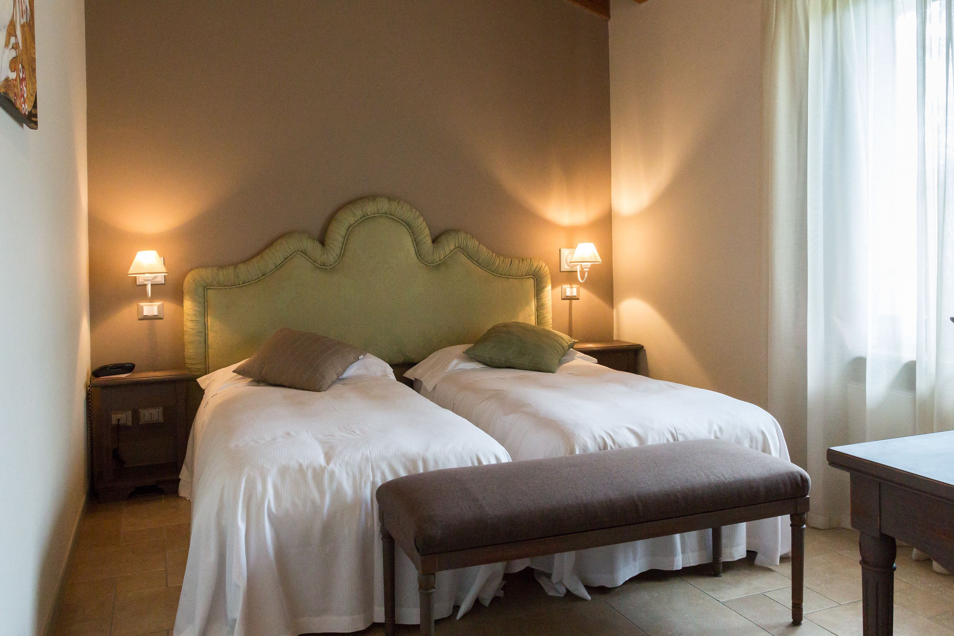 A double bed with a wooden headboard, two bedside tables with lamps, and a bench.