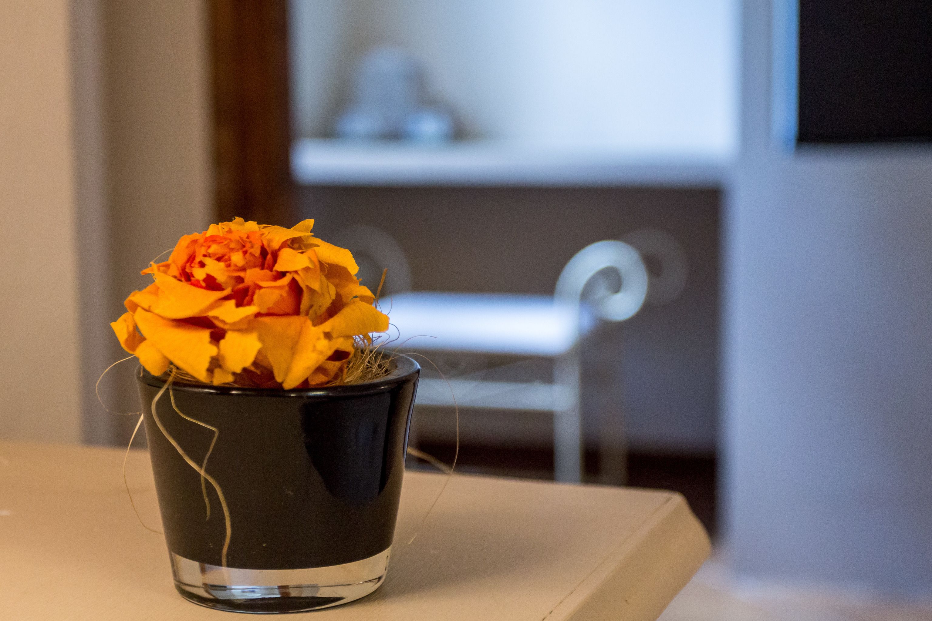A black vase with a yellow flower on a table.