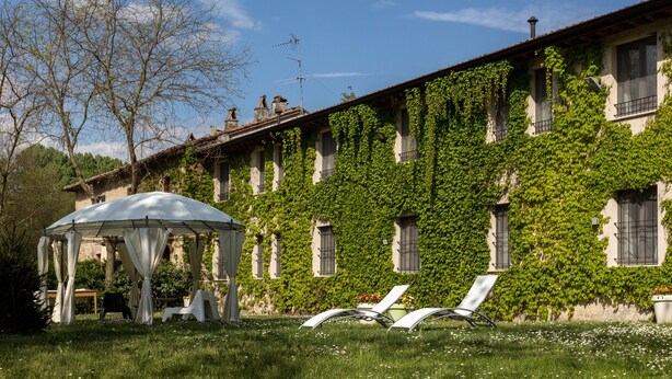 Un bâtiment dont les murs sont recouverts de lierre et qui dispose d’un espace extérieur abrité avec des chaises.