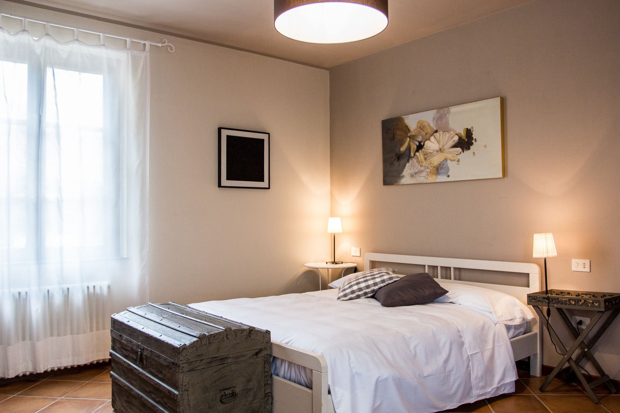 Une chambre à coucher bien rangée, avec un lit, des lampes de chevet, un tableau encadré au mur et une commode rustique.