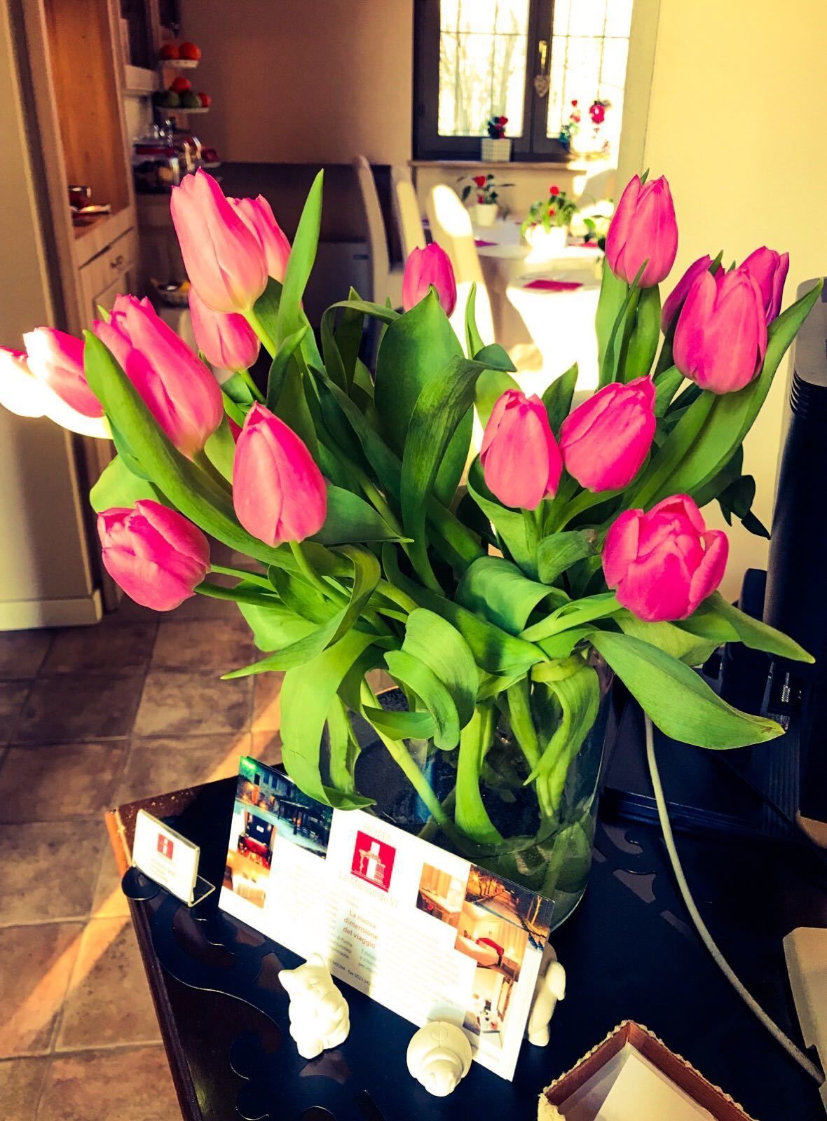 Un bouquet de tulipes roses dans un vase, posé sur une table avec un menu et un petit objet décoratif.