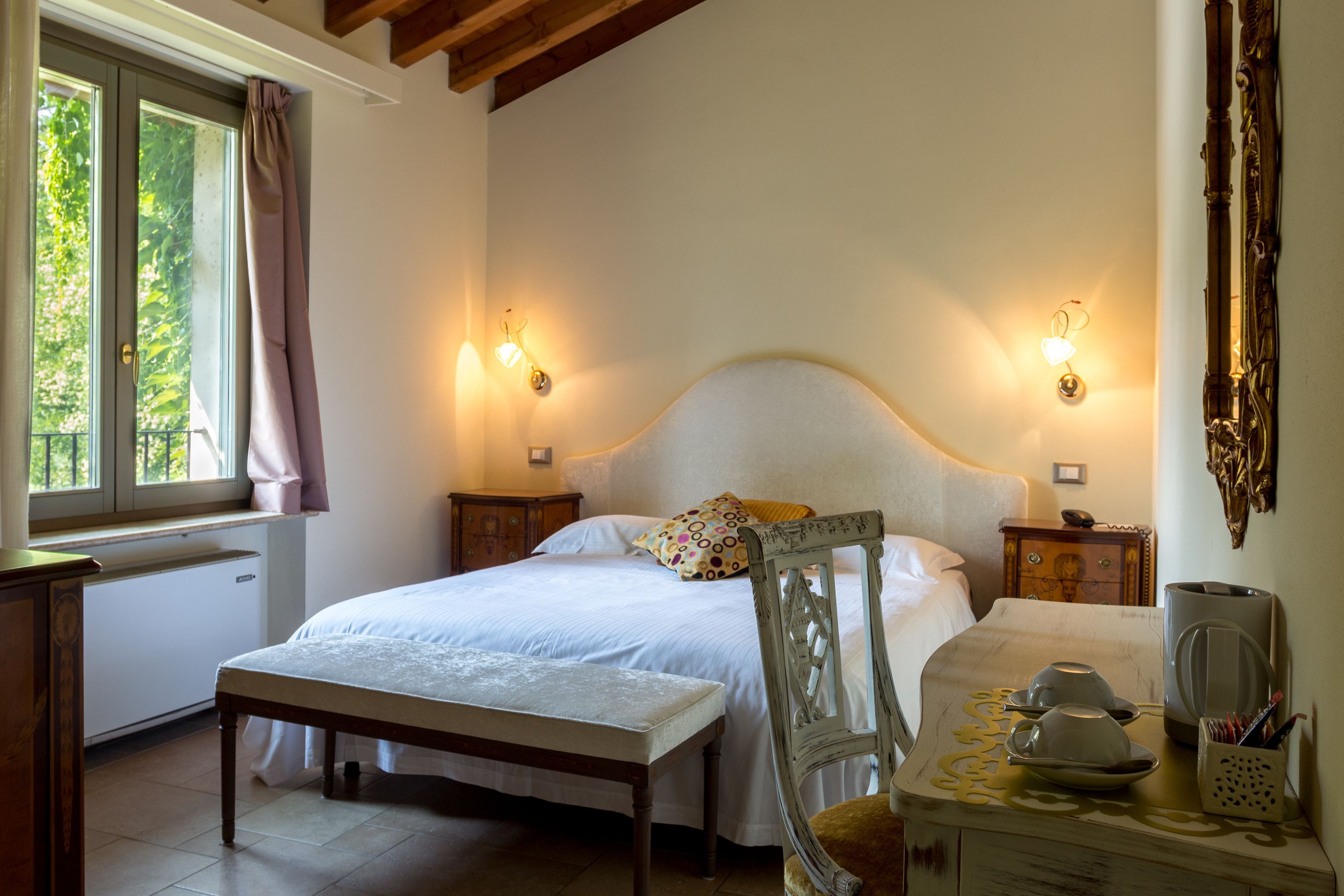 A bedroom with a bed, bedside tables, a chair, a desk, and a window with curtains.