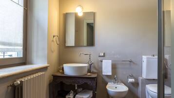 A bathroom with a large window, a sink, a bidet, and a toilet.