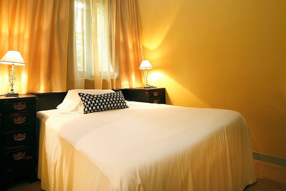 Een hotelkamer met een bed, twee nachtkastjes met lampen, een raam met gordijnen en een gele muur.