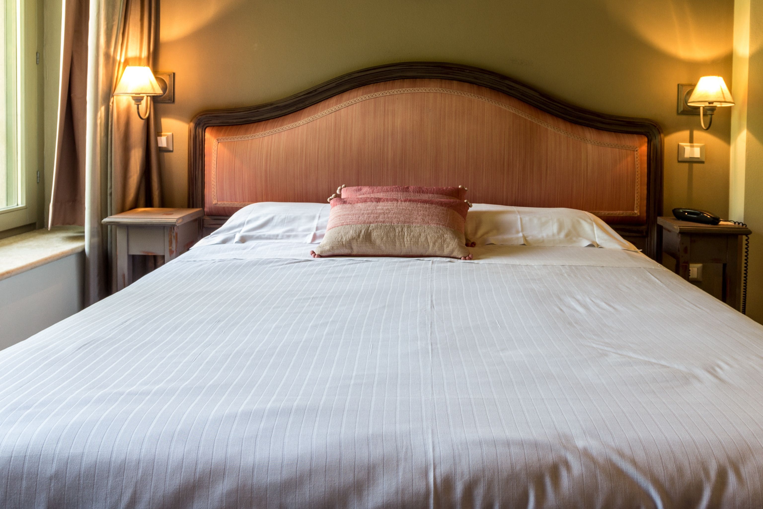 Una cama bien hecha con una colcha a rayas, dos lámparas de noche y un cabecero de madera.