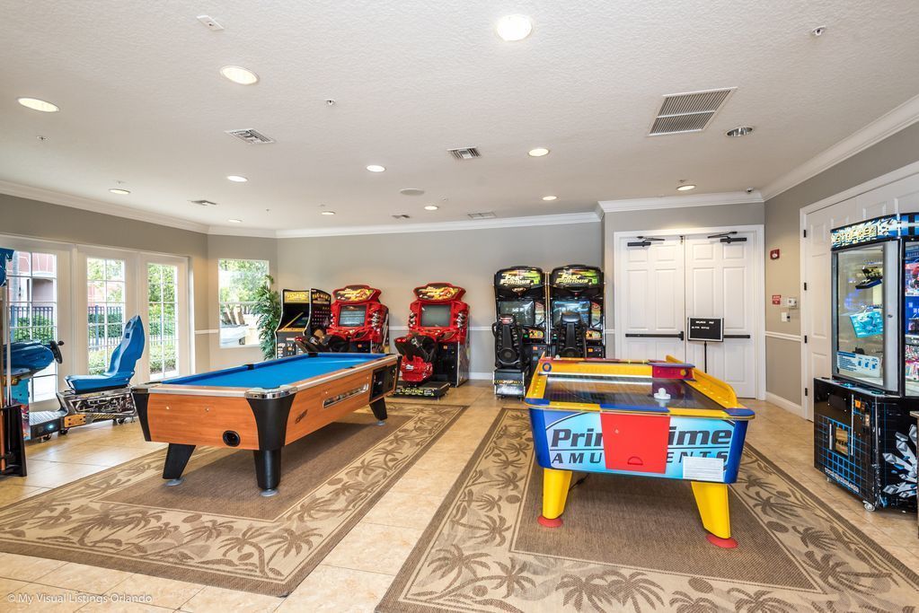 A pool table, arcade games, and a billiards table in a room with patterned carpet and large windows.
