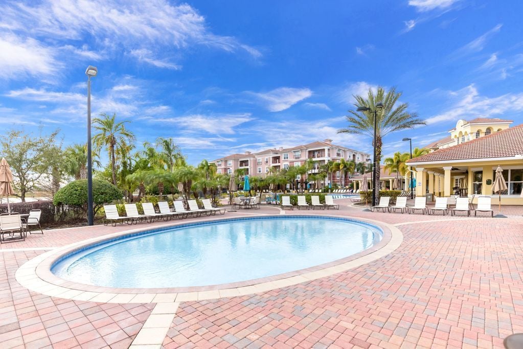 A swimming pool with lounge chairs and palm trees, surrounded by buildings with balconies.
