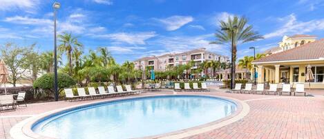 A swimming pool with lounge chairs and palm trees, surrounded by buildings with balconies.