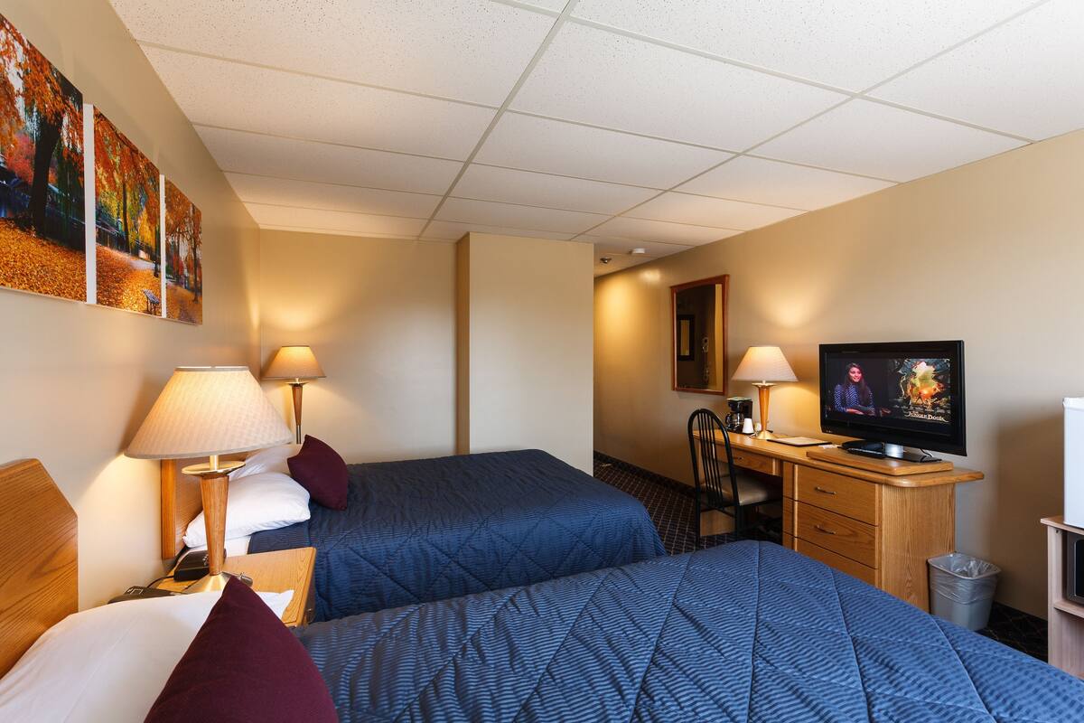 A hotel room with two beds, a desk, a television, and a trash can.