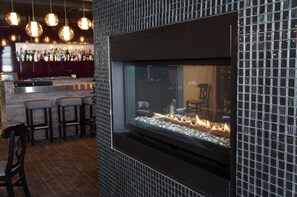 Zona de bar con chimenea, taburetes y lámparas colgantes.