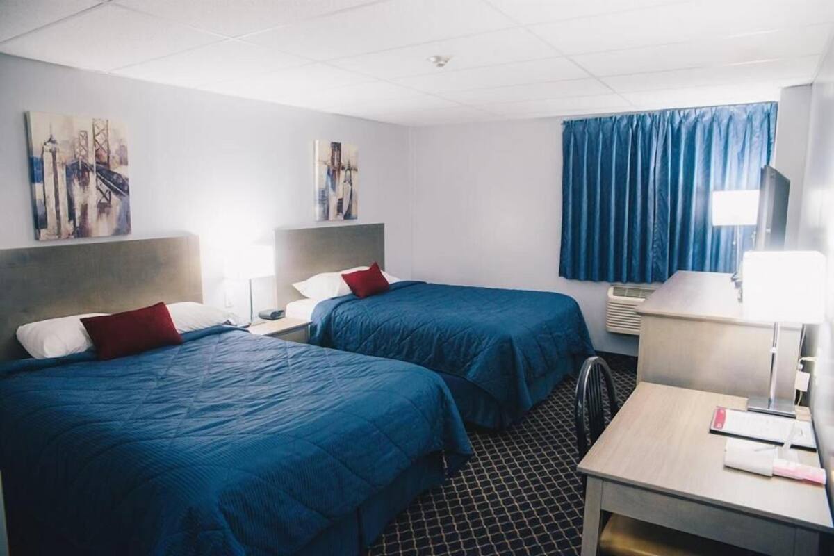 A hotel room with two beds, a desk, a chair, a TV, and artwork on the walls.
