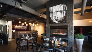 En restaurang med en bardel, bord, stolar och en stor krukväxt.