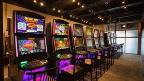 En rad spelautomater i ett svagt upplyst rum med heltäckningsmatta på golvet och ett stort fönster i bakgrunden.
