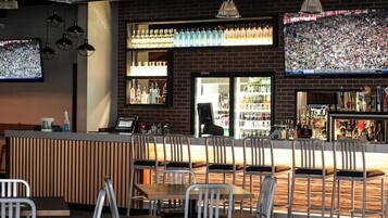 A bar area with a counter, multiple seating options, and a television screen displaying a sports event.
