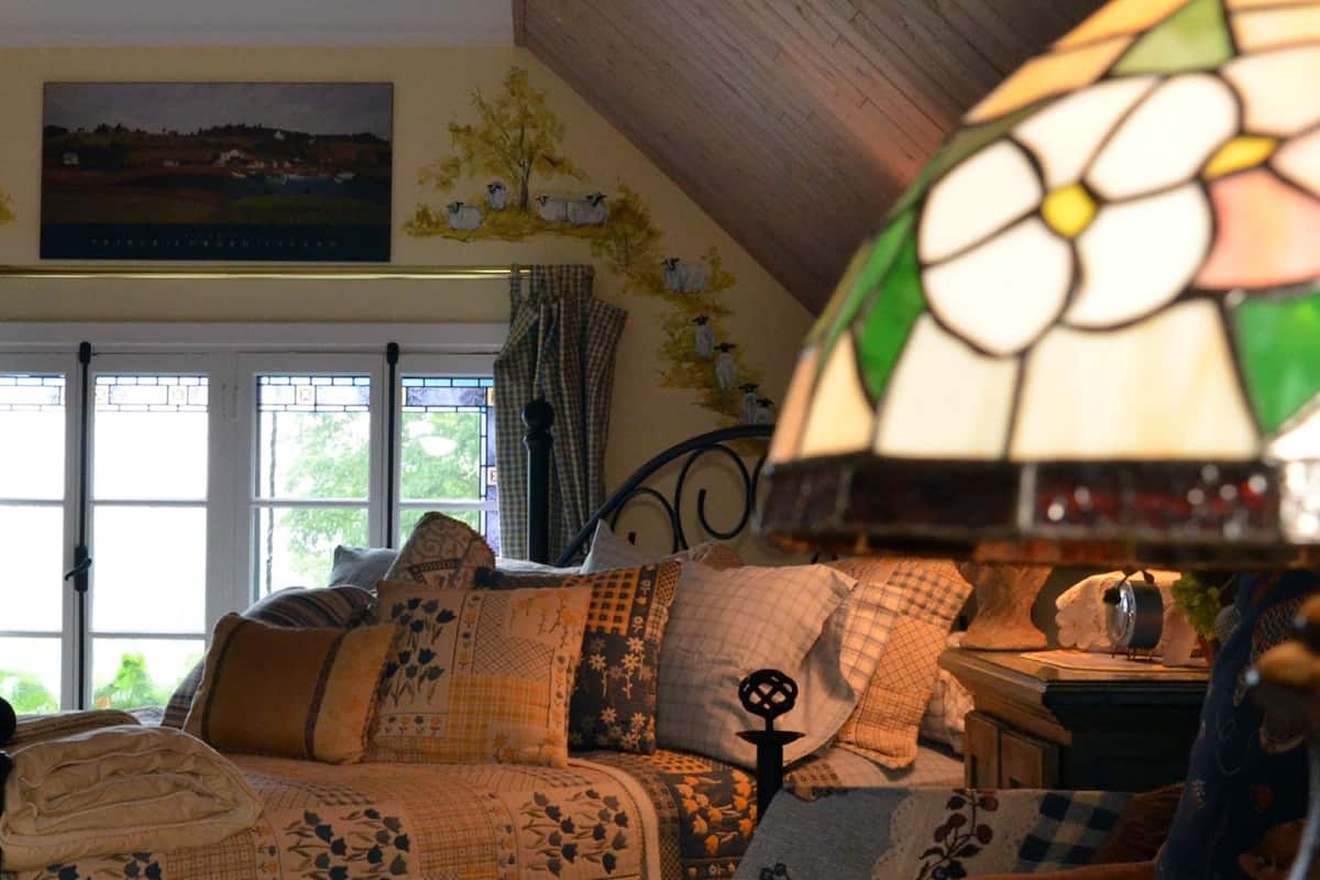 A cozy bedroom with a bed, a stained glass lamp, and a window with curtains.