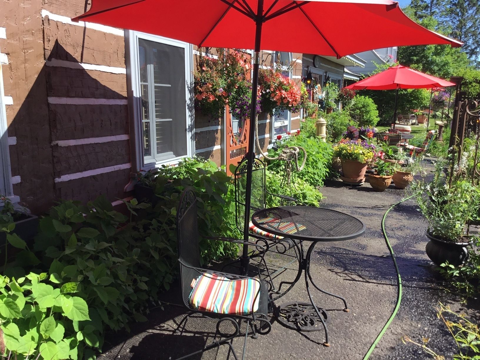 A patio area with a metal table and chairs, surrounded by potted plants and a red umbrella.