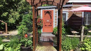 Un arco de madera que conduce a una puerta con diseño decorativo, rodeada de abundante follaje y una planta en maceta.
