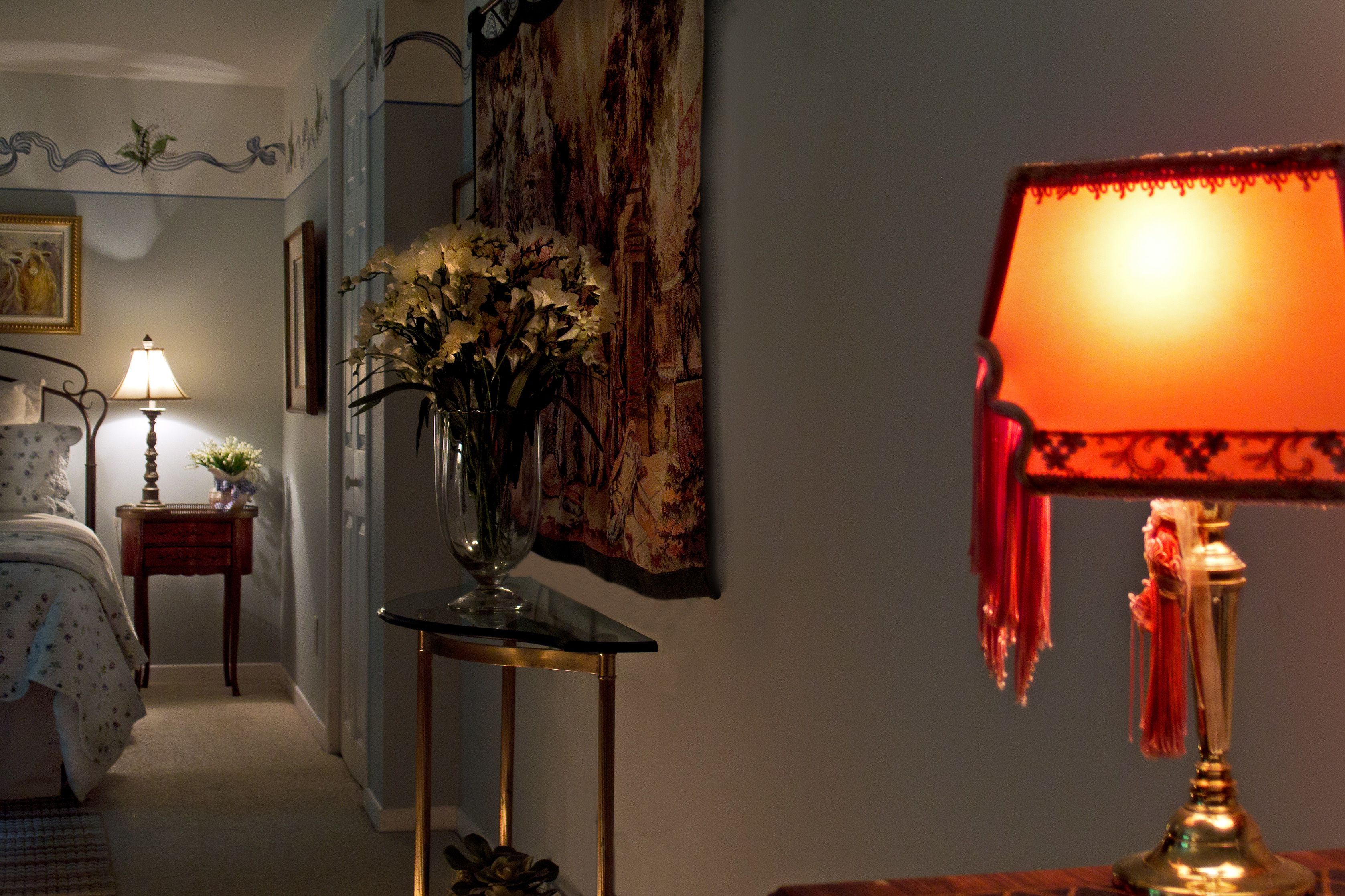 Une chambre à coucher avec un lit, une table de chevet avec une lampe, un vase de fleurs et un tableau accroché au mur.