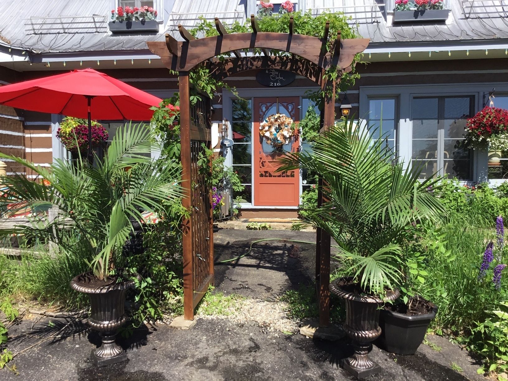 A garden entrance with a wooden archway, potted plants, and a red umbrella.