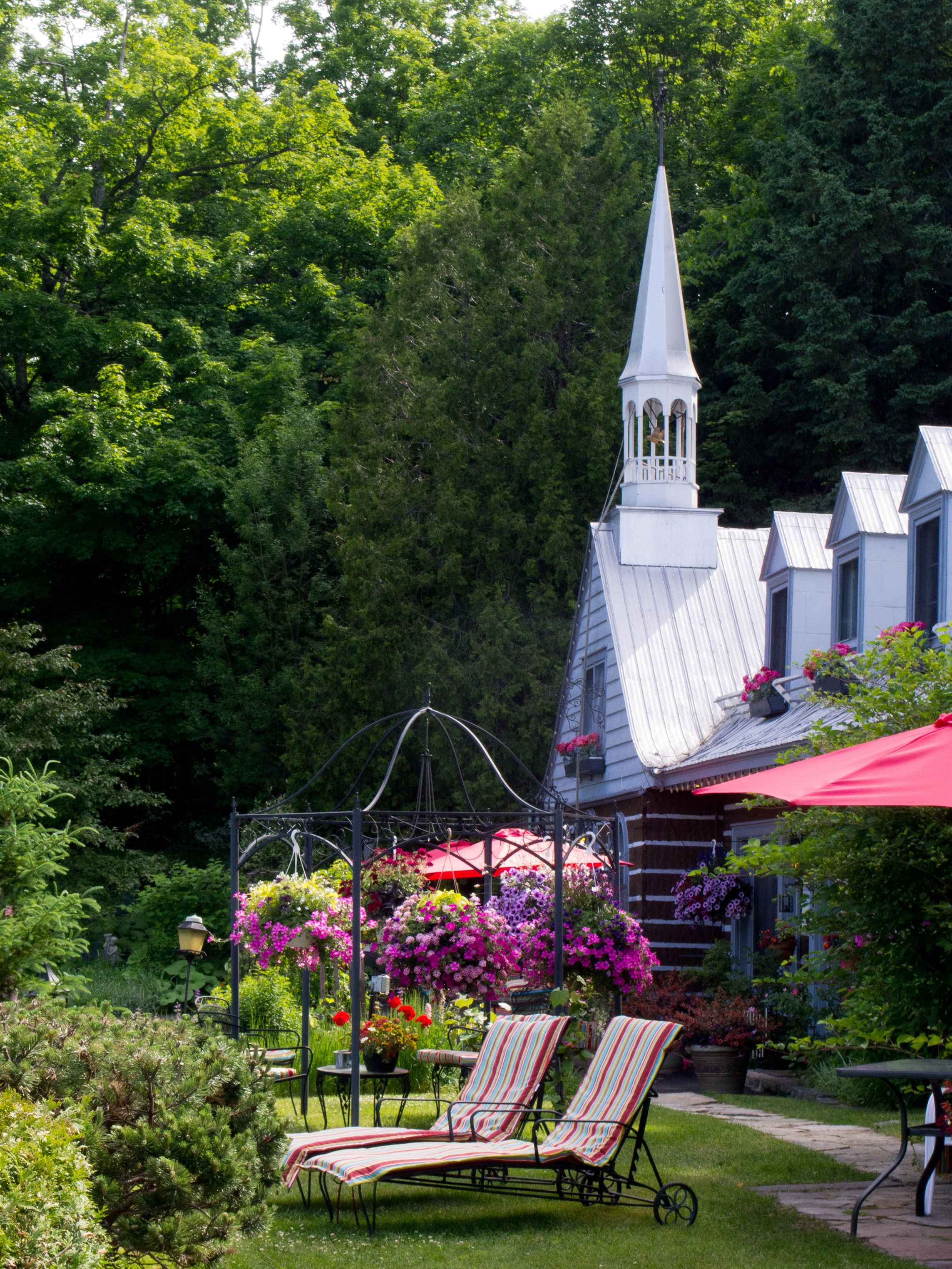 A garden with a gazebo, lounge chairs, and a white building with a steeple.