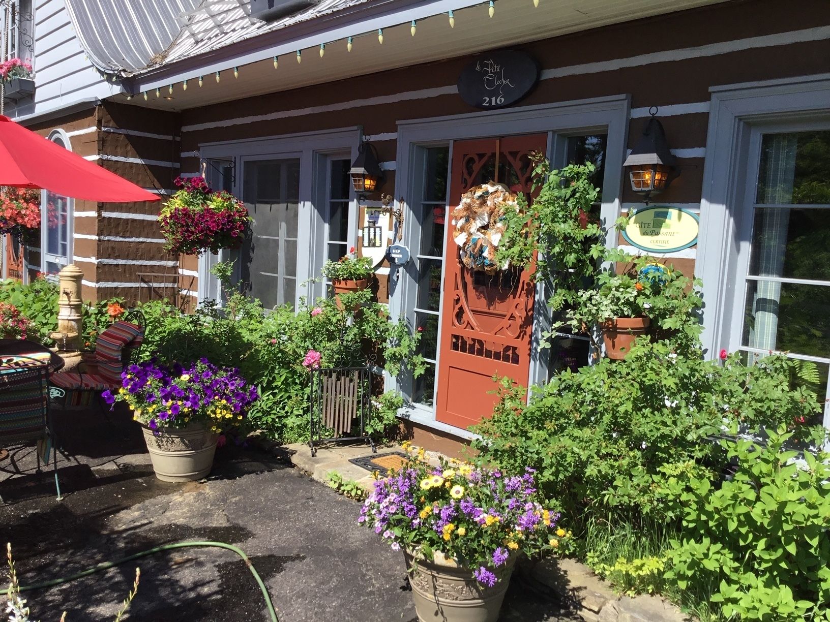 A cozy outdoor seating area with a red umbrella, potted plants, and a stone table.