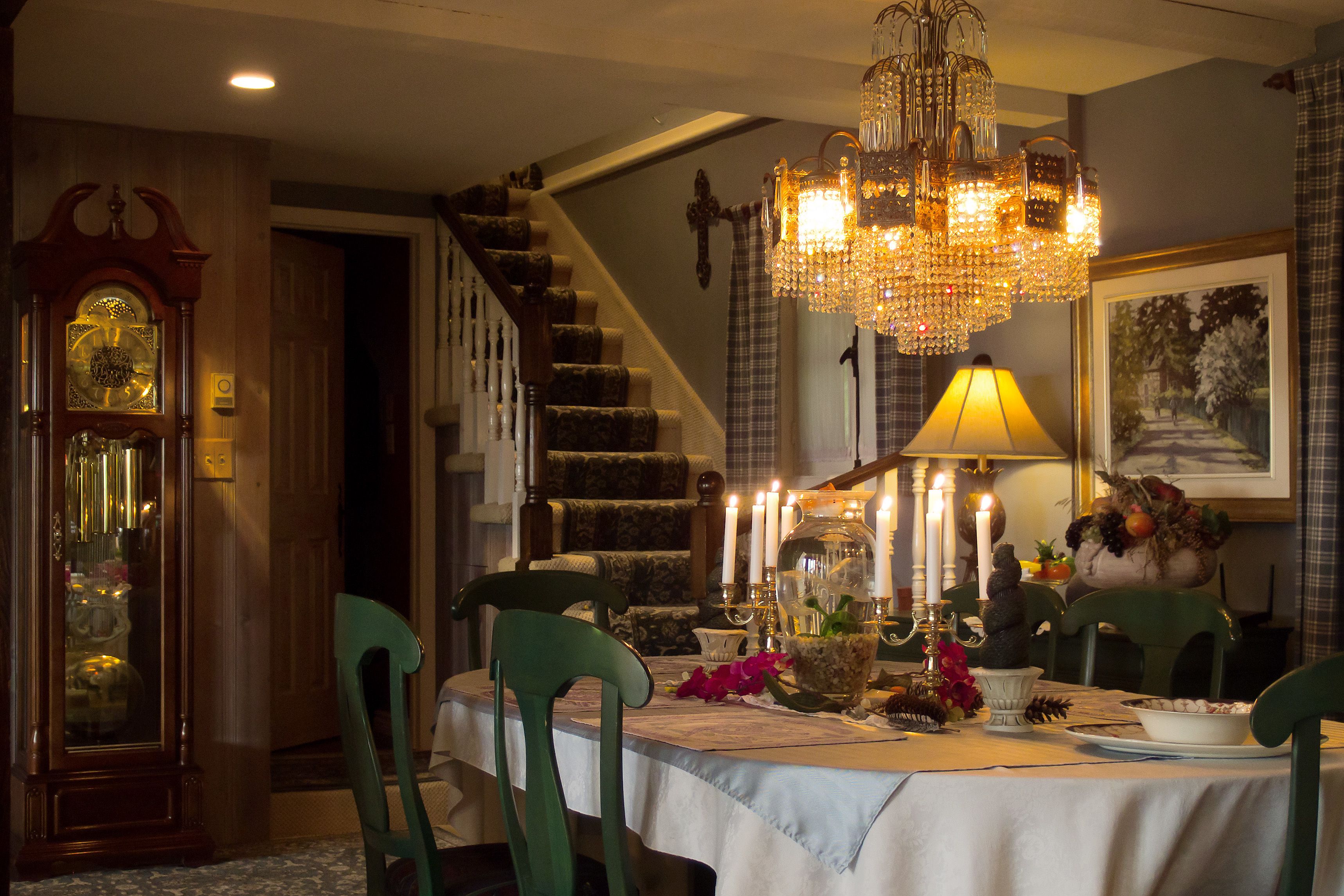 A dining area with a chandelier, table set with candles, and a clock on the wall.
