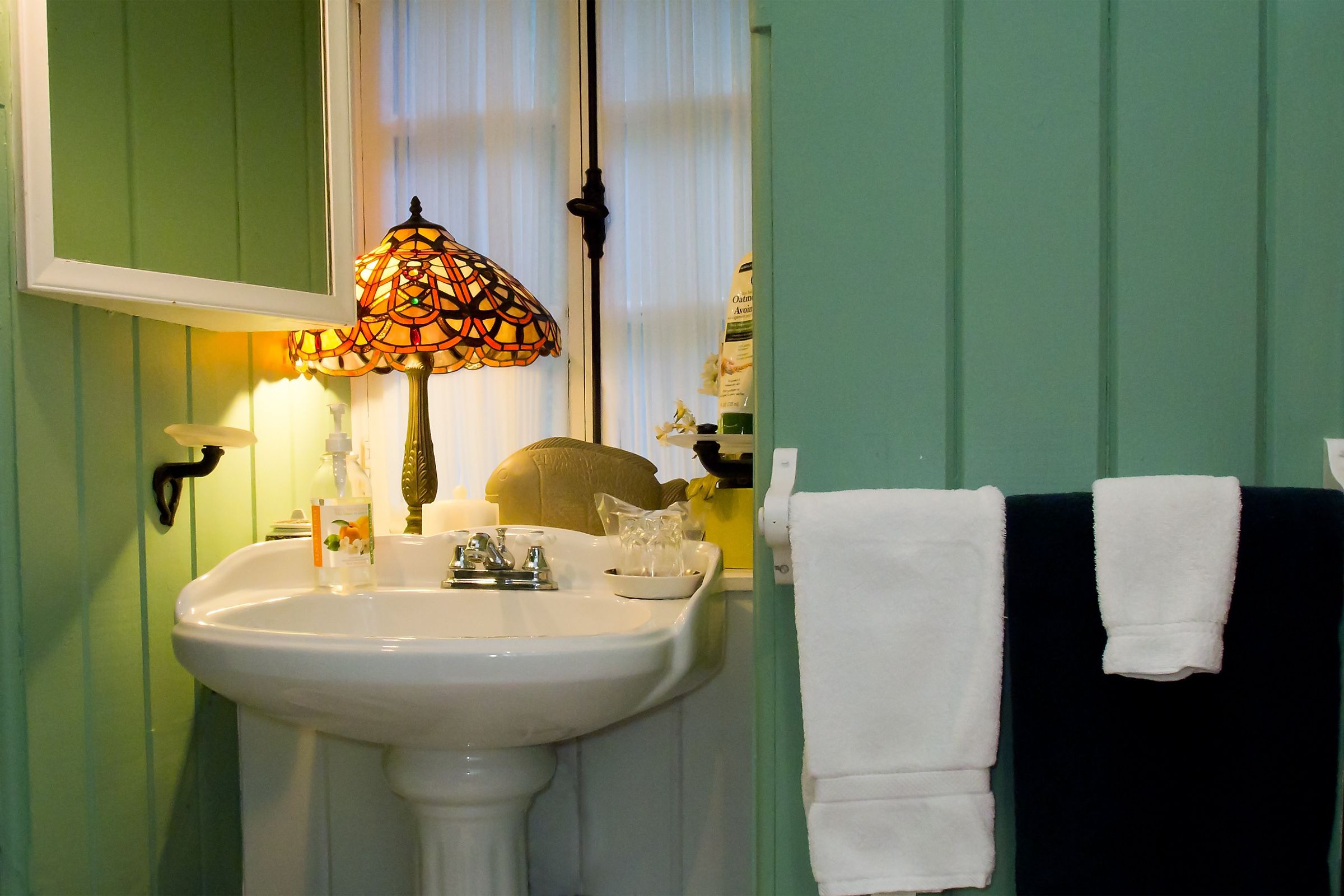 A bathroom with a white sink, a stained glass lamp, and a towel rack with white and black towels.
