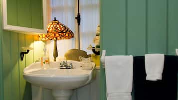 A bathroom with a white sink, a stained glass lamp, and a towel rack with white and black towels.