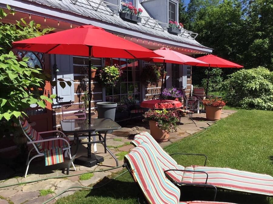 Un patio con mobiliario exterior, incluyendo sillones reclinables a rayas y una mesa con sombrillas rojas.