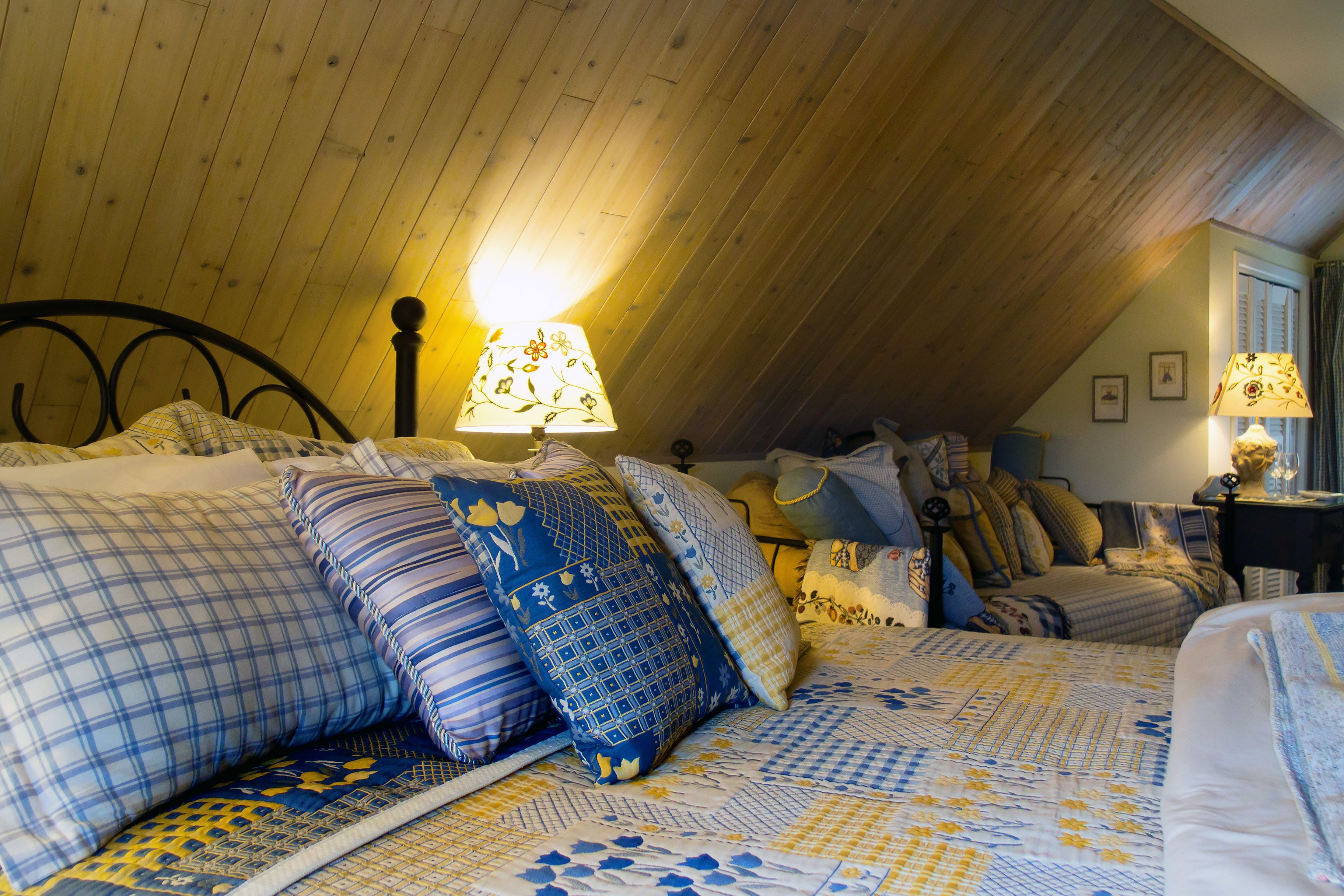 A cozy attic bedroom with a sloped ceiling, a bed with patterned bedding, and two table lamps.