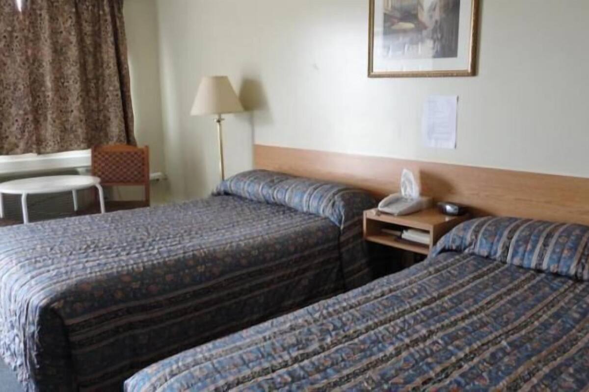 A hotel room with two beds, a desk, a chair, a lamp, and a framed picture on the wall.
