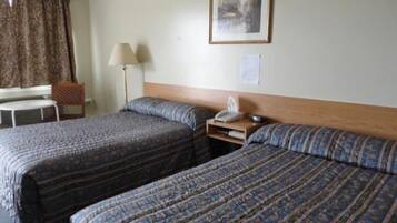 A hotel room with two beds, a desk, a chair, a lamp, and a framed picture on the wall.