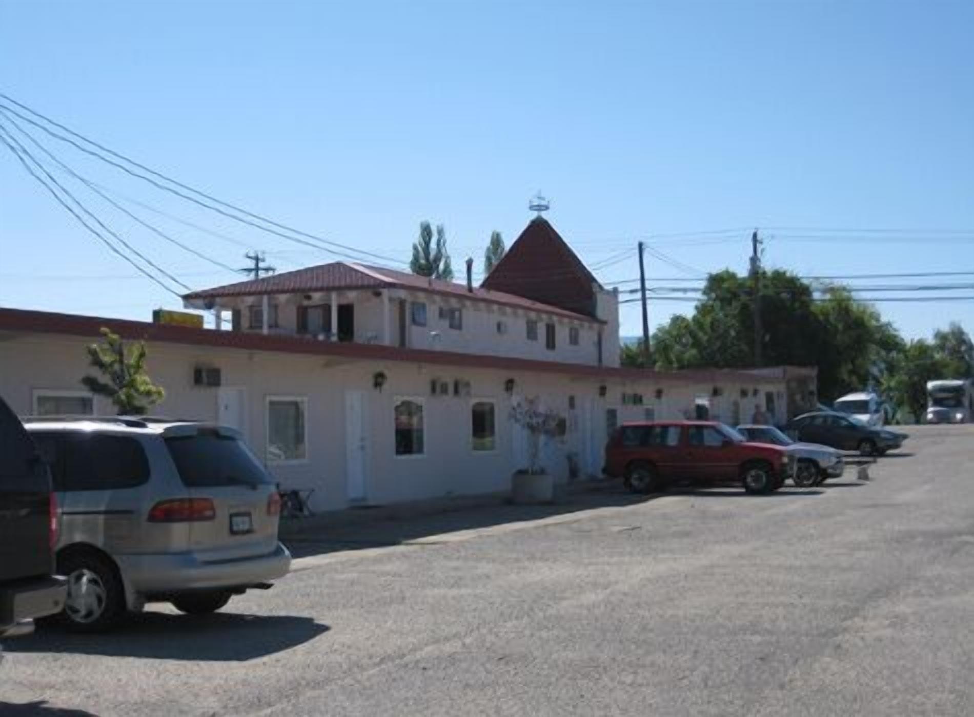 Un edificio con techo rojo y fachada blanca, coches aparcados al frente y líneas eléctricas por encima.