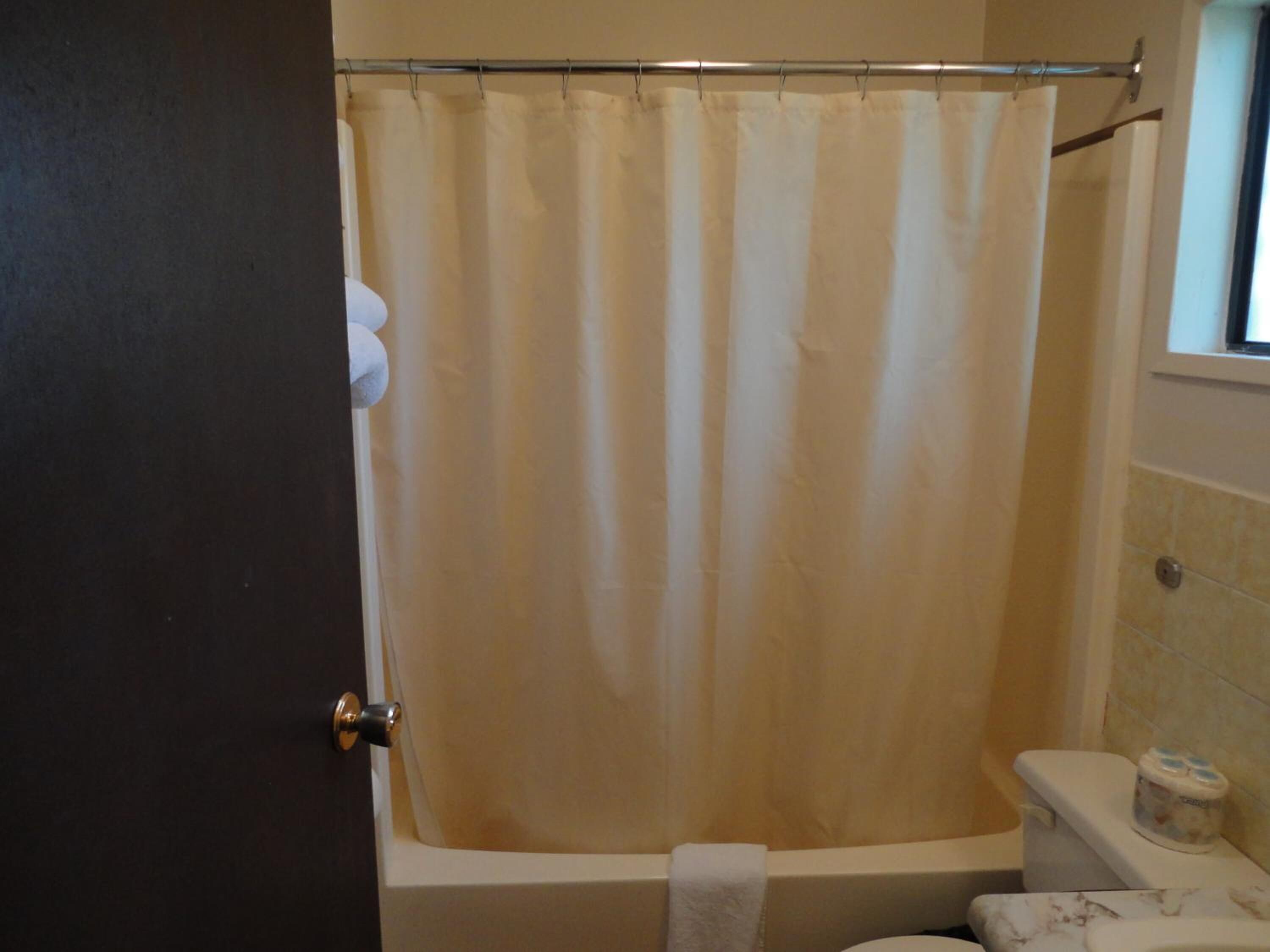 A bathroom with a beige shower curtain, a white bathtub, and a toilet with a marble-like design.