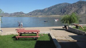 Un espace de pique-nique au bord du lac, avec une table de pique-nique rouge, une pelouse et une vue sur les montagnes en arrière-plan.