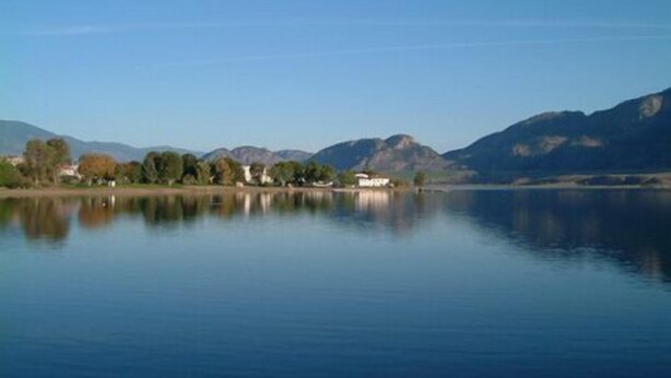 A calm lake with mountains in the background and a few buildings along the shore. - Falcon Resort (Osoyoos)