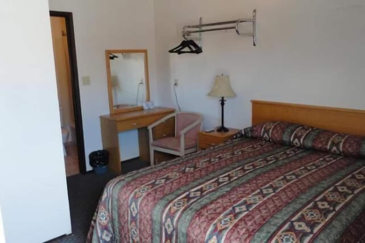 A bedroom with a bed, a desk, a chair, a mirror, and a hanging clothes rack.