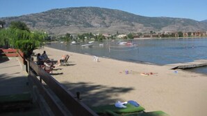 A beach with boats, a mountain in the background, and a few people. - Falcon Resort (Osoyoos)