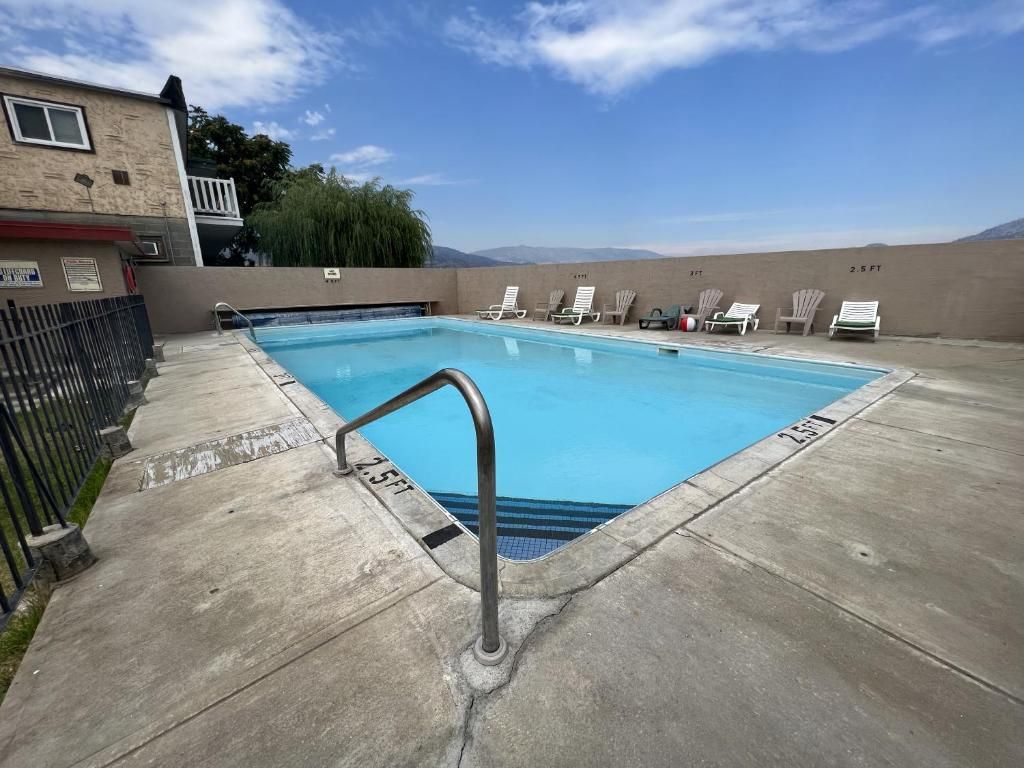 A swimming pool with a metal ladder, lounge chairs, and a view of mountains.