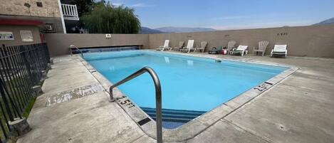 A swimming pool with a metal ladder, lounge chairs, and a view of mountains.