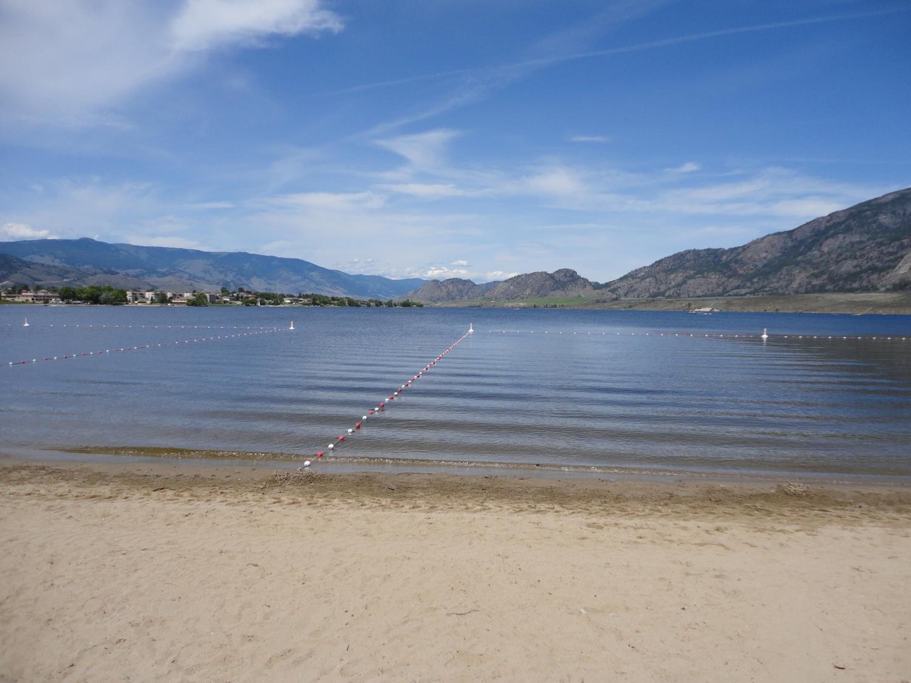 A beach with a clear sky, calm water, and distant mountains.