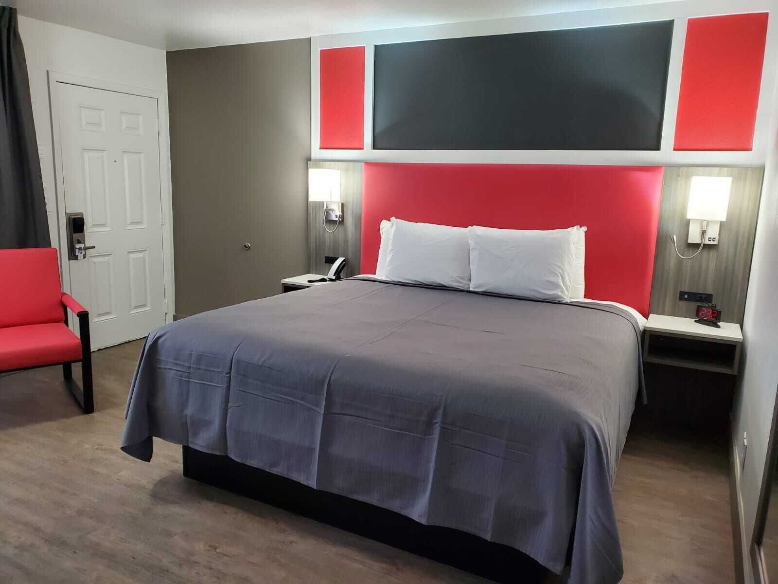 A hotel room with a large bed, a red chair, and a white door.