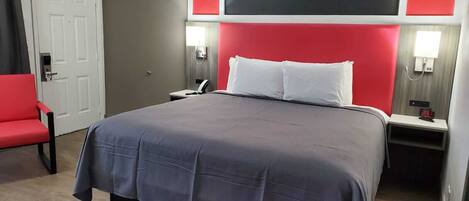 A hotel room with a large bed, a red chair, and a white door.