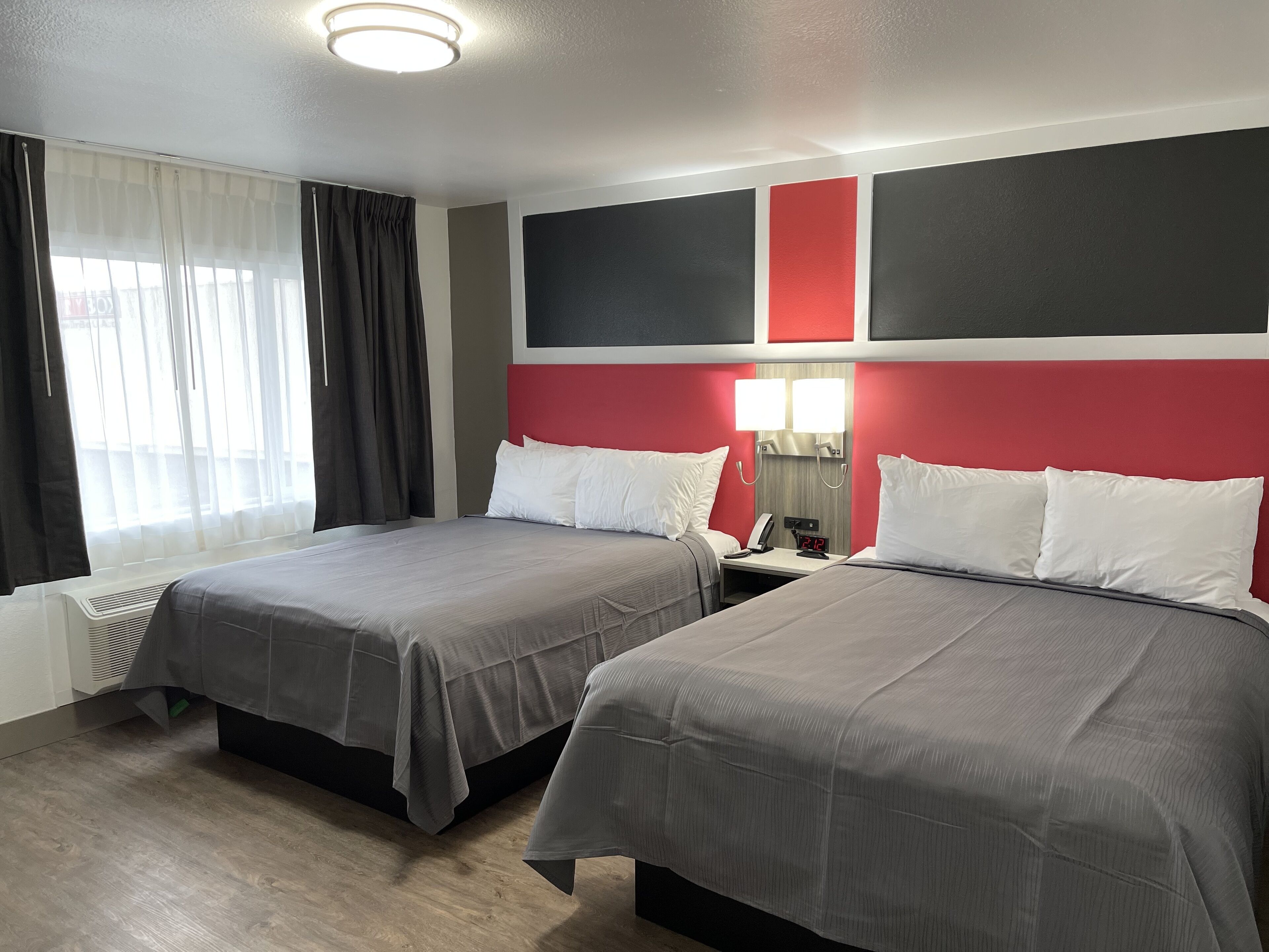 A hotel room with two beds, a nightstand with a lamp, and a window with curtains.