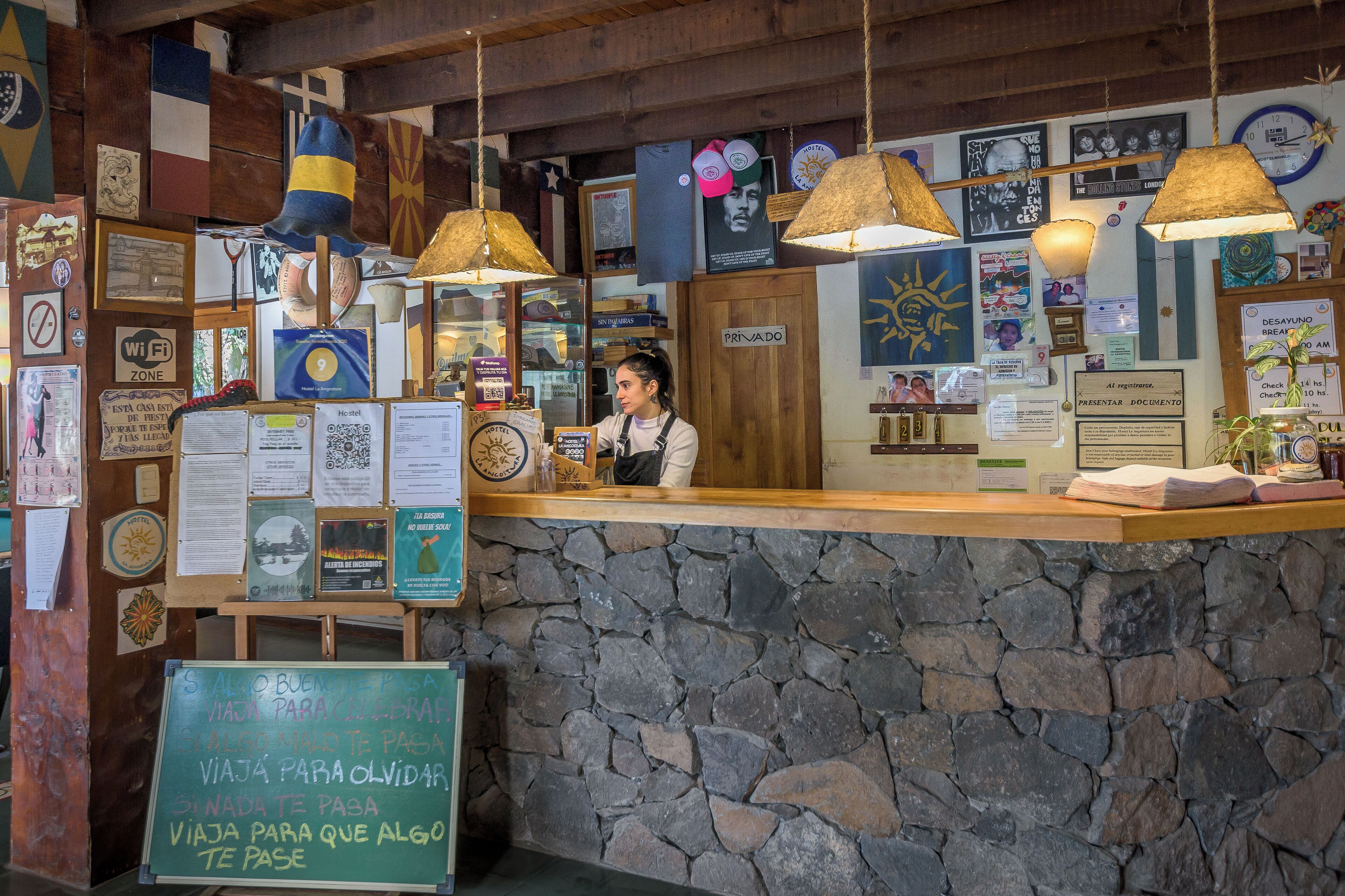 Interior rústico com parede de pedra, teto de madeira e diversas decorações, incluindo bandeiras e placas.